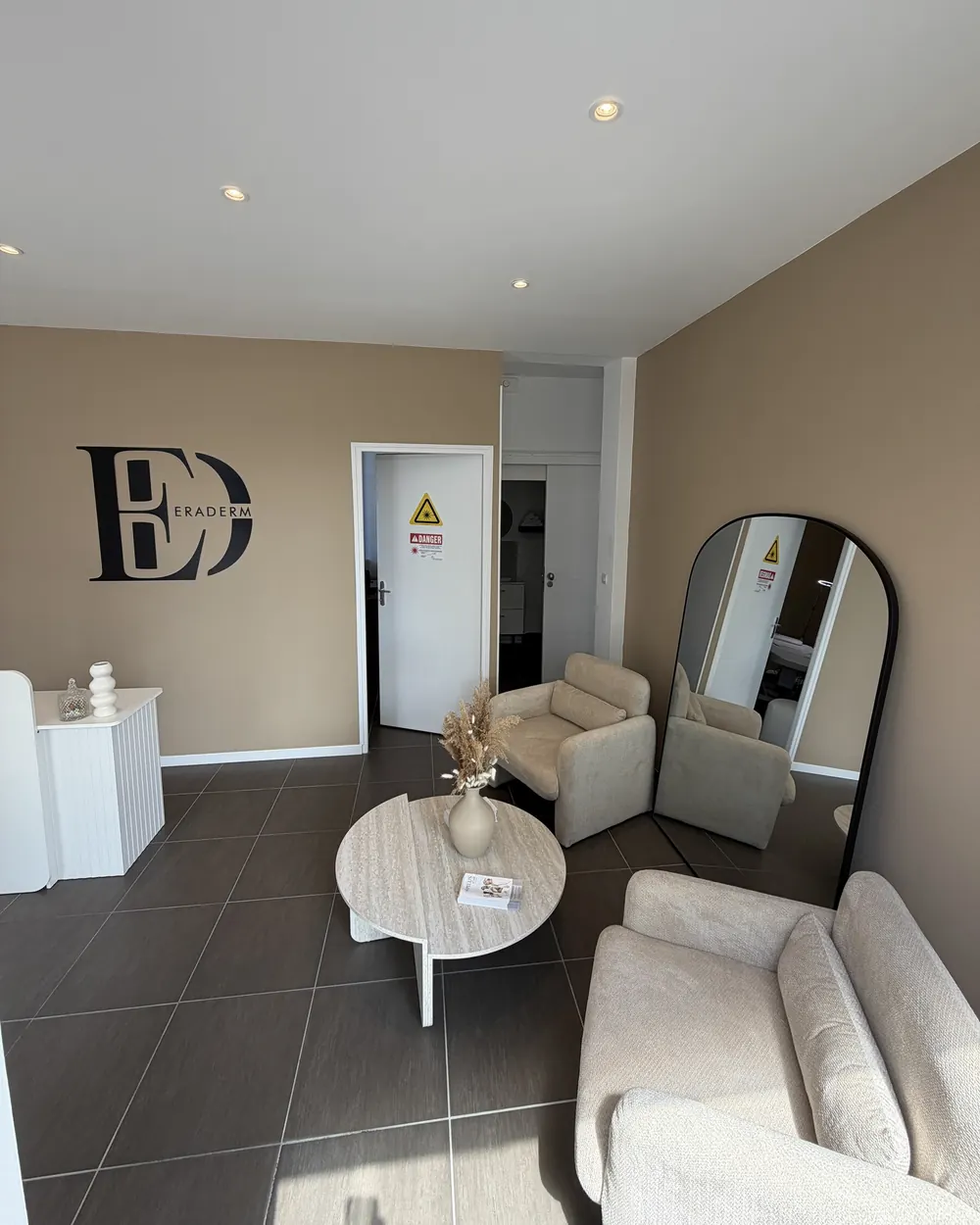 Salon d'attente du cabinet : fauteuils clairs, table basse, logo ERADERM au mur